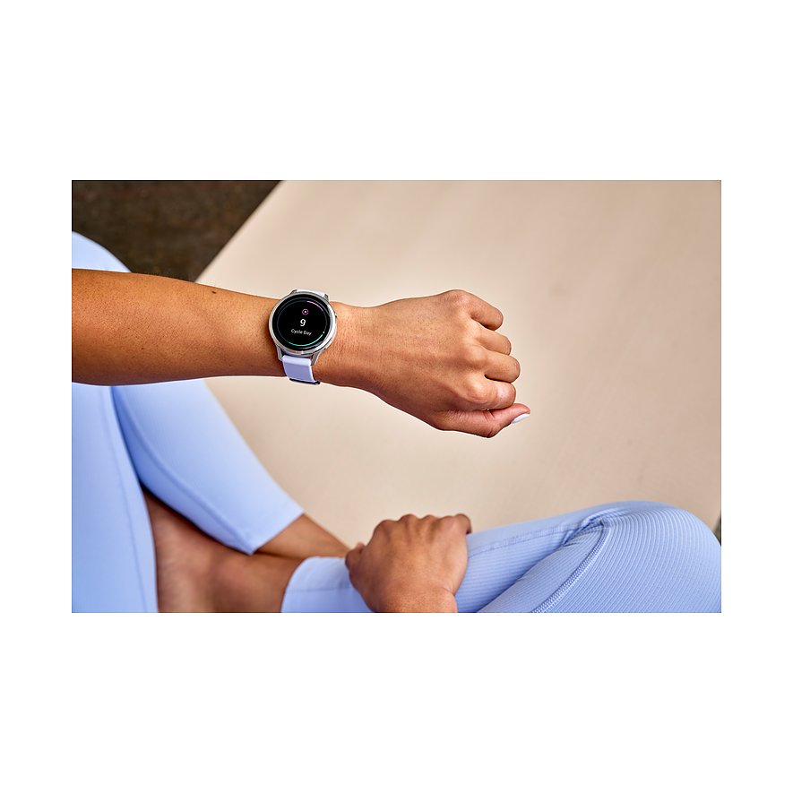 Eine Frau trägt eine Garmin Smartwatch aus Kunststoff mit lila Band und silbernem Gehäuse an ihrem Arm.
