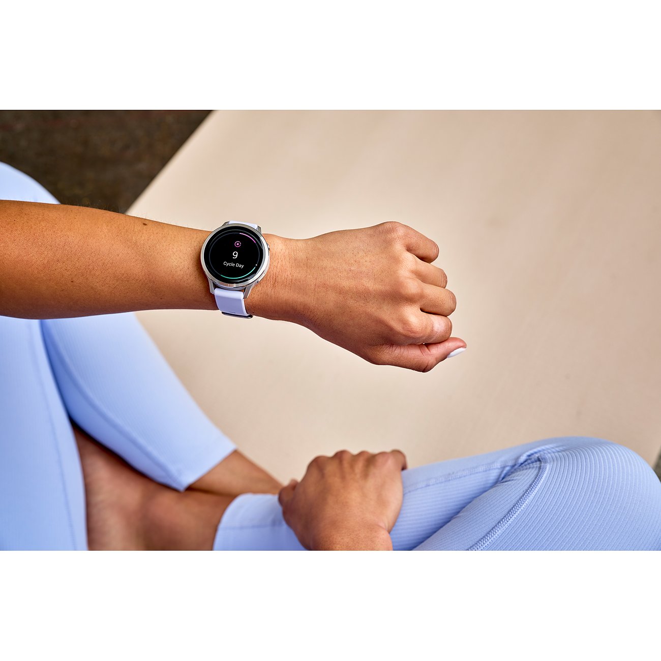 Eine Frau trägt eine Garmin Smartwatch aus Kunststoff mit lila Band und silbernem Gehäuse an ihrem Arm.
