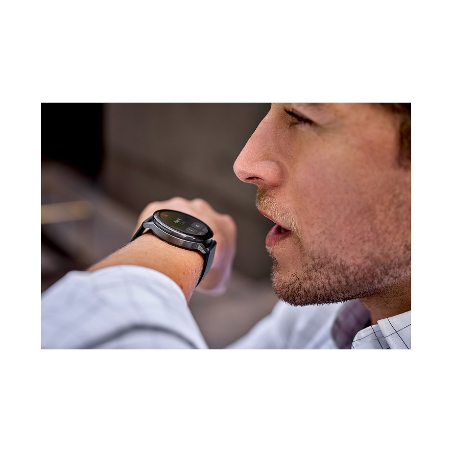 Ein Mann mit Bart trägt eine Garmin Smartwatch aus Kunststoff und blickt auf das Display an seinem linken Handgelenk.