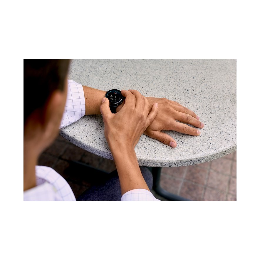 Eine Person sitzt an einem Tisch und blickt auf die Garmin Smartwatch aus Kunststoff.