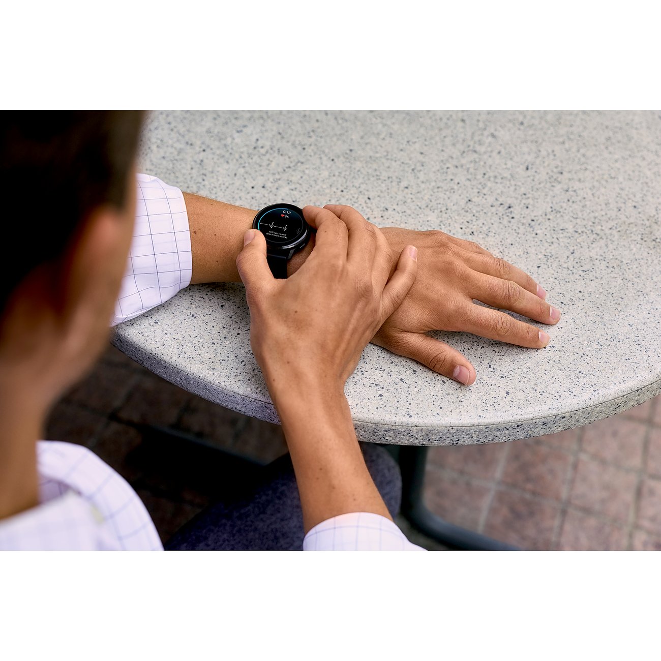 Eine Person sitzt an einem Tisch und blickt auf die Garmin Smartwatch aus Kunststoff.