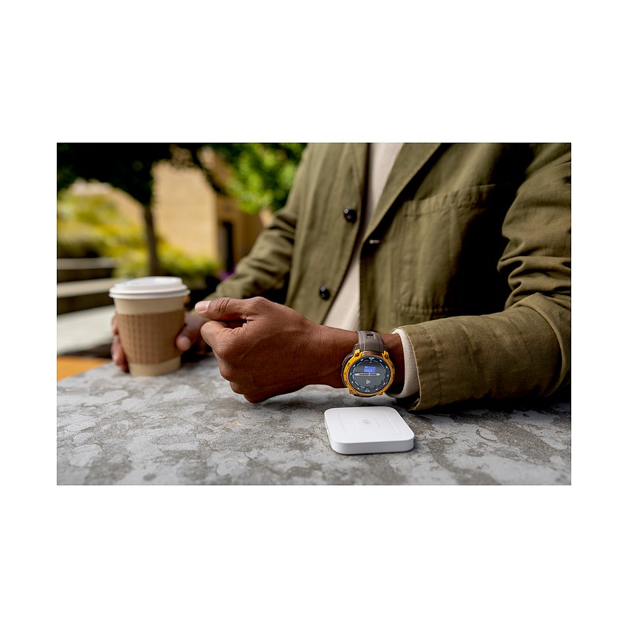 Ein Garmin Smartwatch aus Kunststoff am Handgelenk einer Person mit einem Kaffeebecher auf einem Tisch.