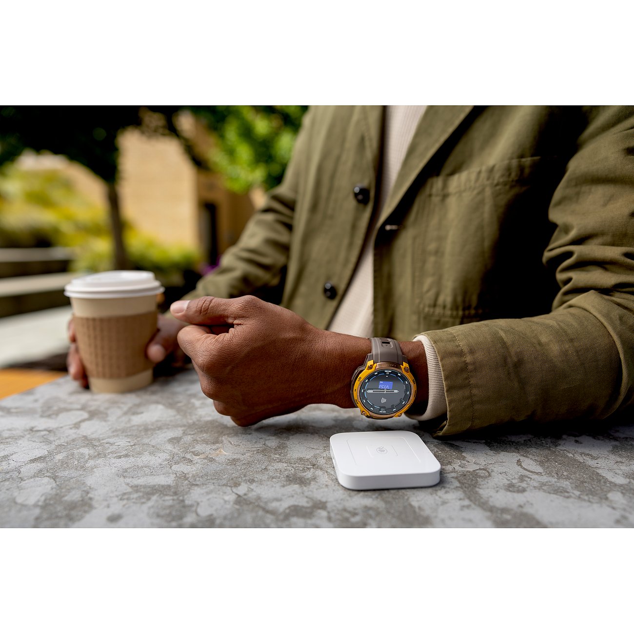 Ein Garmin Smartwatch aus Kunststoff am Handgelenk einer Person mit einem Kaffeebecher auf einem Tisch.