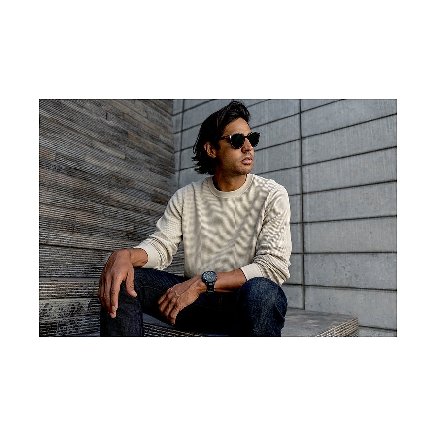 Ein Mann trägt eine Garmin Smartwatch aus Kunststoff und sitzt mit Sonnenbrille und Jeans lässig auf einer Treppe.