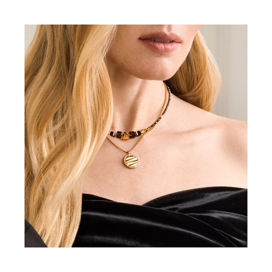 Gros plan d'une femme avec un collier Coeur de Lion en acier inoxydable doré, gemmes brunes et pendentif rond.