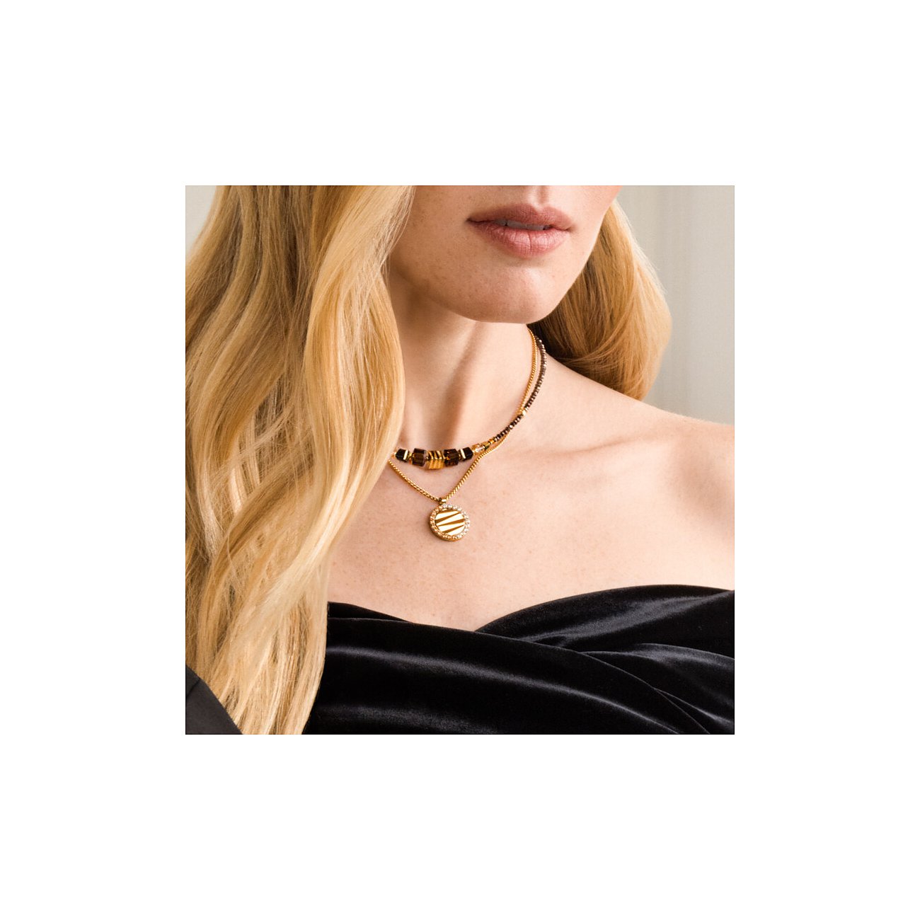 Gros plan d'une femme avec un collier Coeur de Lion en acier inoxydable doré, gemmes brunes et pendentif rond.