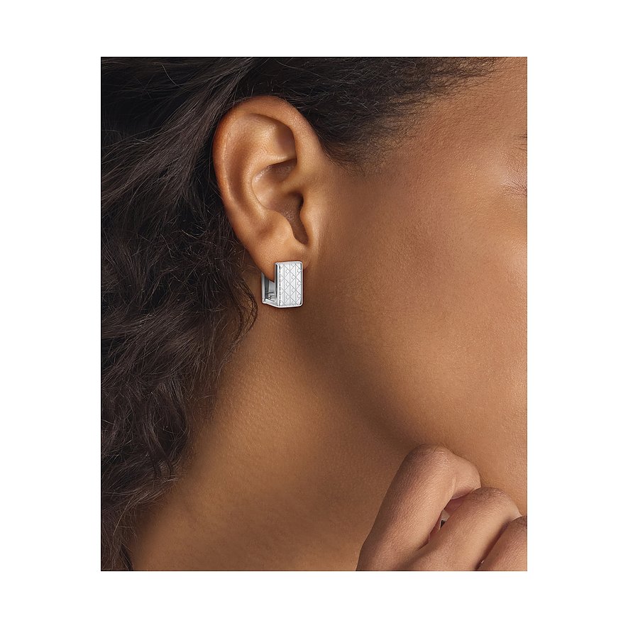 Ein Calvin Klein Ohrring aus Edelstahl ist am Ohr getragen zu sehen. Er ist halbmondförmig mit einem Muster.