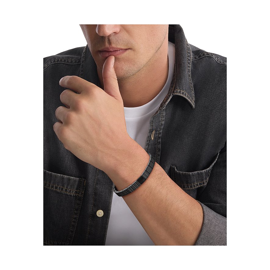 Nahaufnahme eines Mannes, der ein Calvin Klein Armband aus Edelstahl trägt, Arm auf dem Schoß, Hand am Kinn.