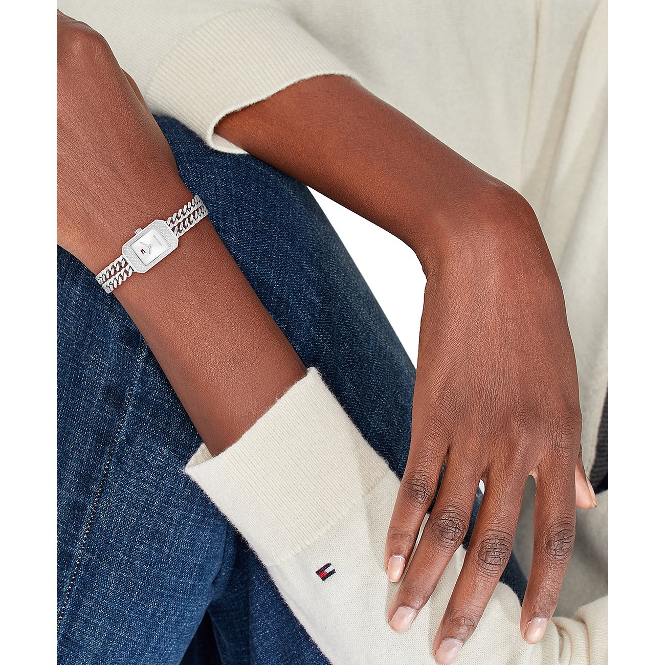 Am Handgelenk getragene Tommy Hilfiger Damenuhr aus Edelstahl mit eckigem Zifferblatt und glitzernden Details.