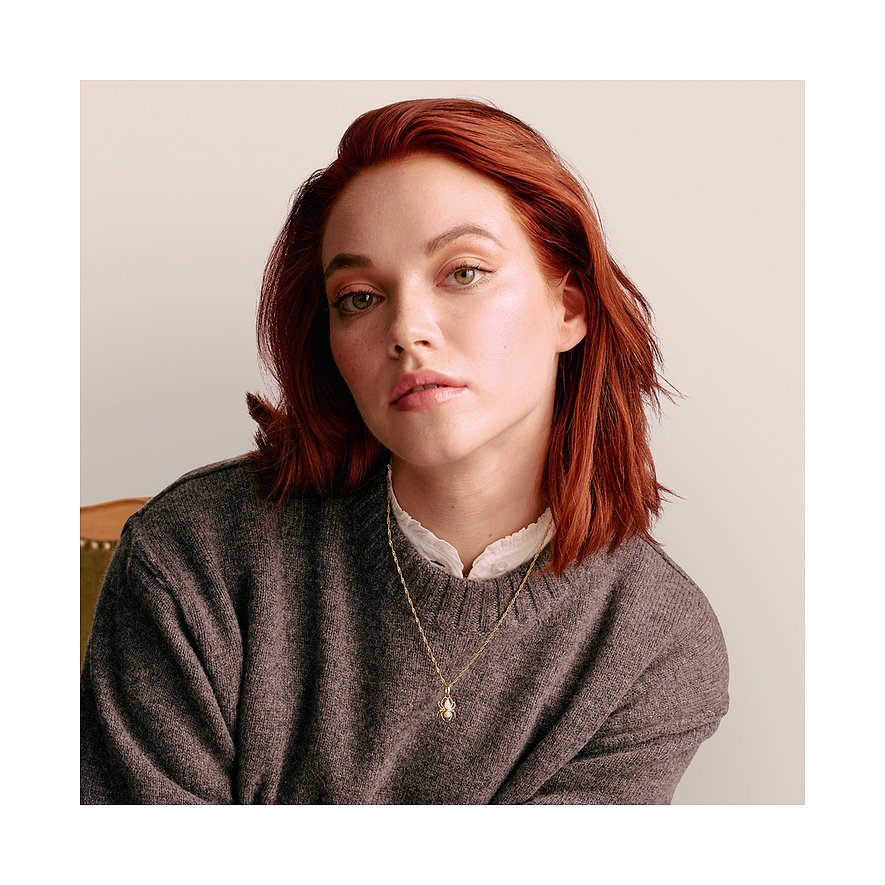 Eine Frau mit roten Haaren trägt eine vergoldete Thomas Sabo Kette mit Zirkonia-Anhänger aus 925er Silber.