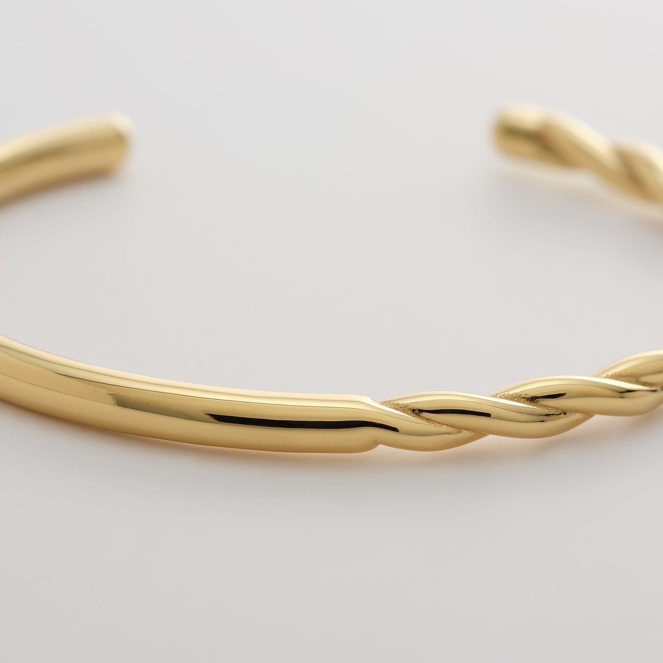 Gros plan d'un bracelet jonc doré Guido Maria Kretschmer en acier, mi-lisse, mi-torsadé.