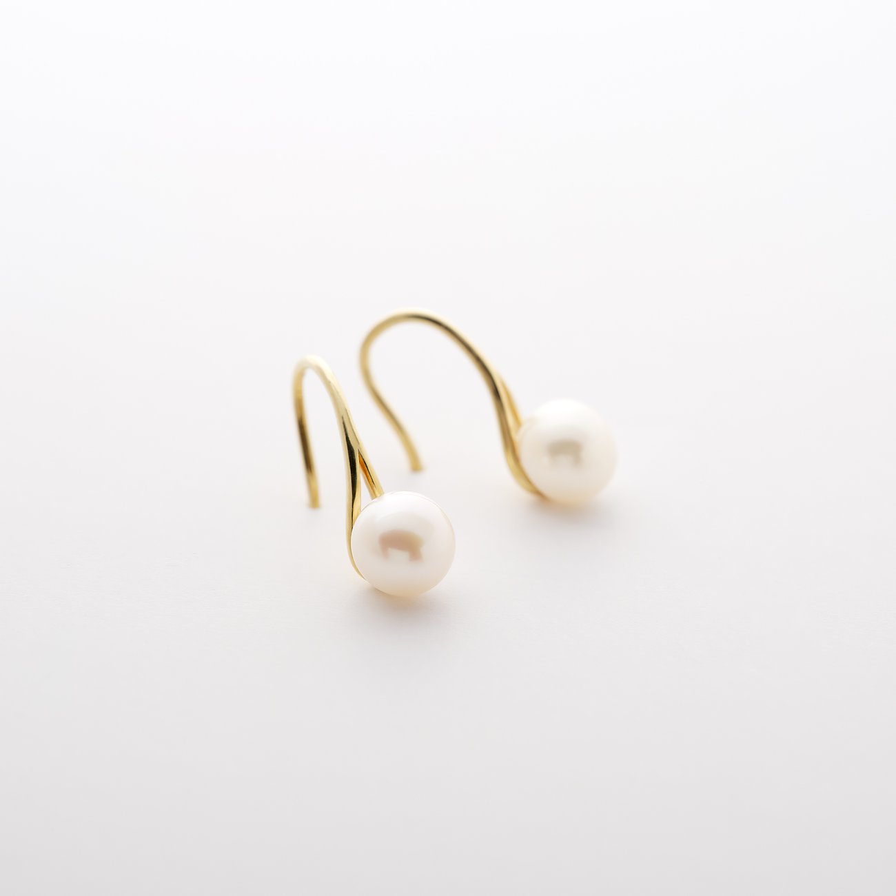 Une paire de boucles d'oreilles CHRIST en or jaune 585, chacune avec une perle blanche, pendant en diagonale.