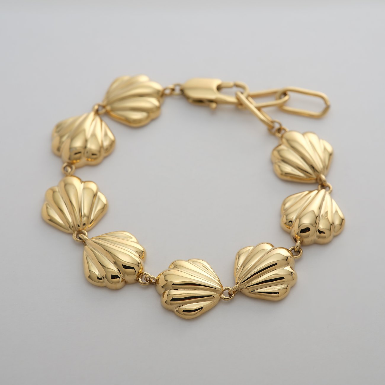 Un bracelet doré Guido Maria Kretschmer en acier inoxydable avec des éléments de coquillage artistiques.