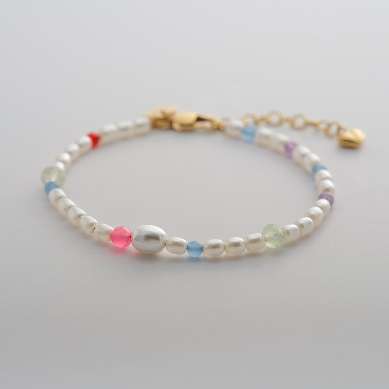 Närbild av Guido Maria Kretschmer armband i rostfritt stål med vita pärlor och färgglada glasstenar.