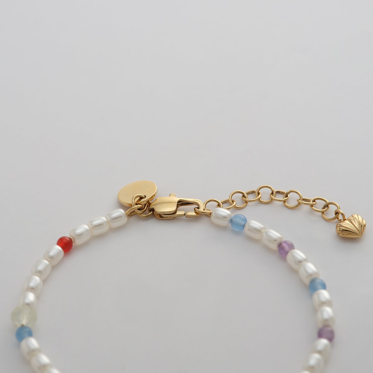 Guido Maria Kretschmer armband: guldfärgat rostfritt stål med vita pärlor och färgglada glasstenar, närbild.