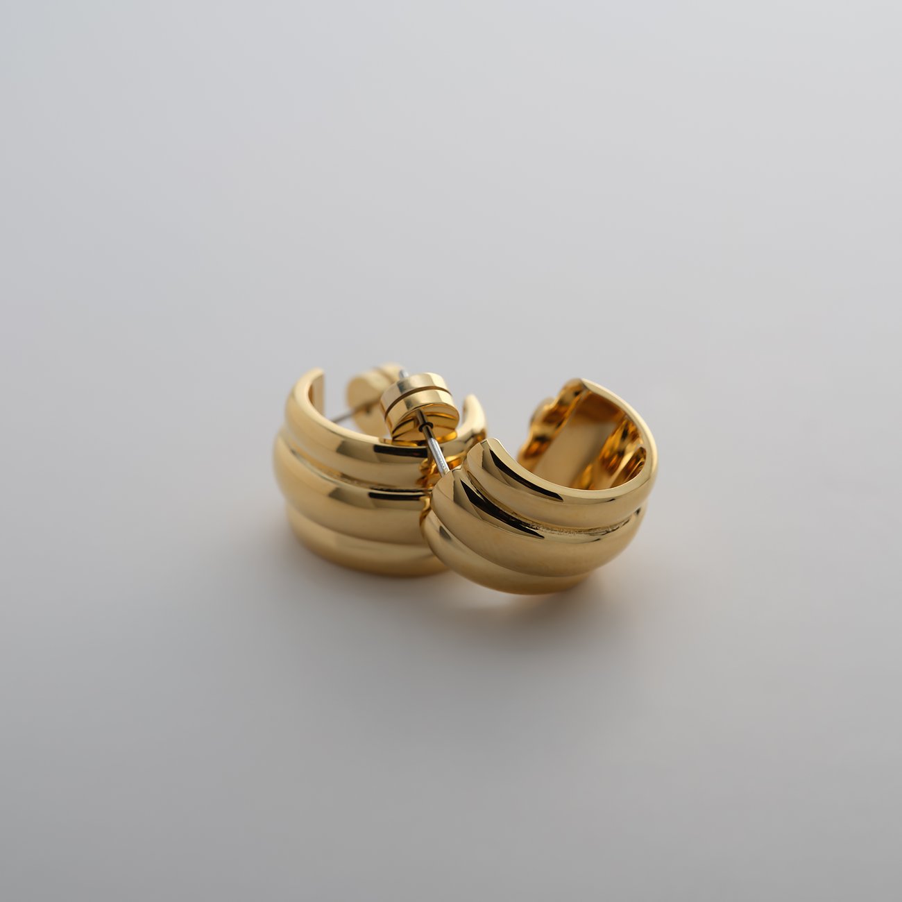 Ein glänzendes, gerilltes Guido Maria Kretschmer Creolen-Paar aus goldenem Edelstahl auf hellem Hintergrund.