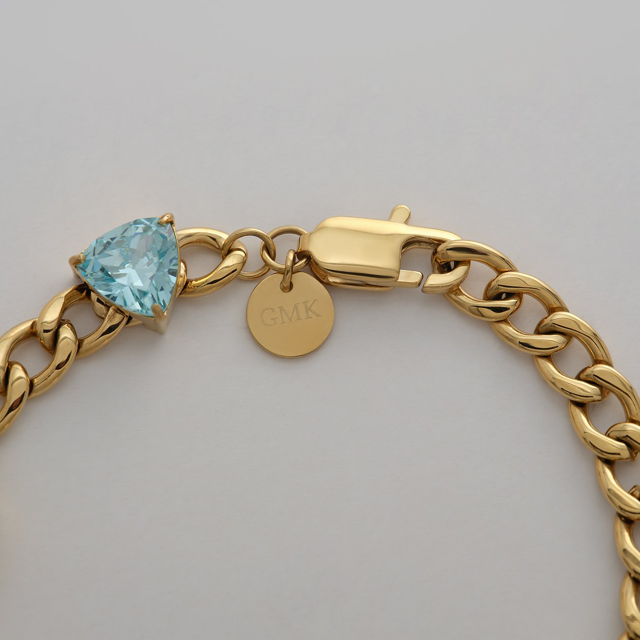 Guido Maria Kretschmer Armschmuck aus goldfarbenem Edelstahl mit hellblauem dreieckigem Zirkonia-Farbstein.