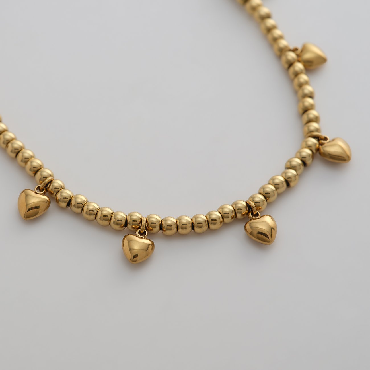 Primo piano di un bracciale dorato Guido Maria Kretschmer in acciaio inox con piccole perle e ciondoli a cuore.