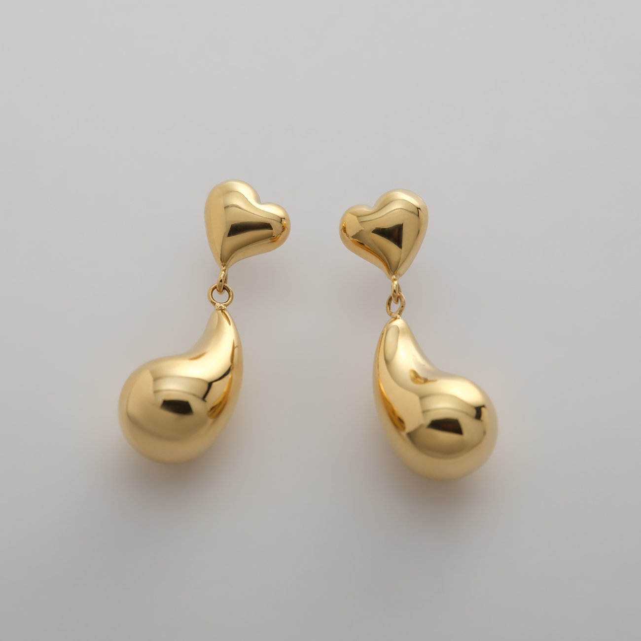 Une paire de boucles d'oreilles pendantes Guido Maria Kretschmer couleur or en acier, cœur en haut, goutte en bas.