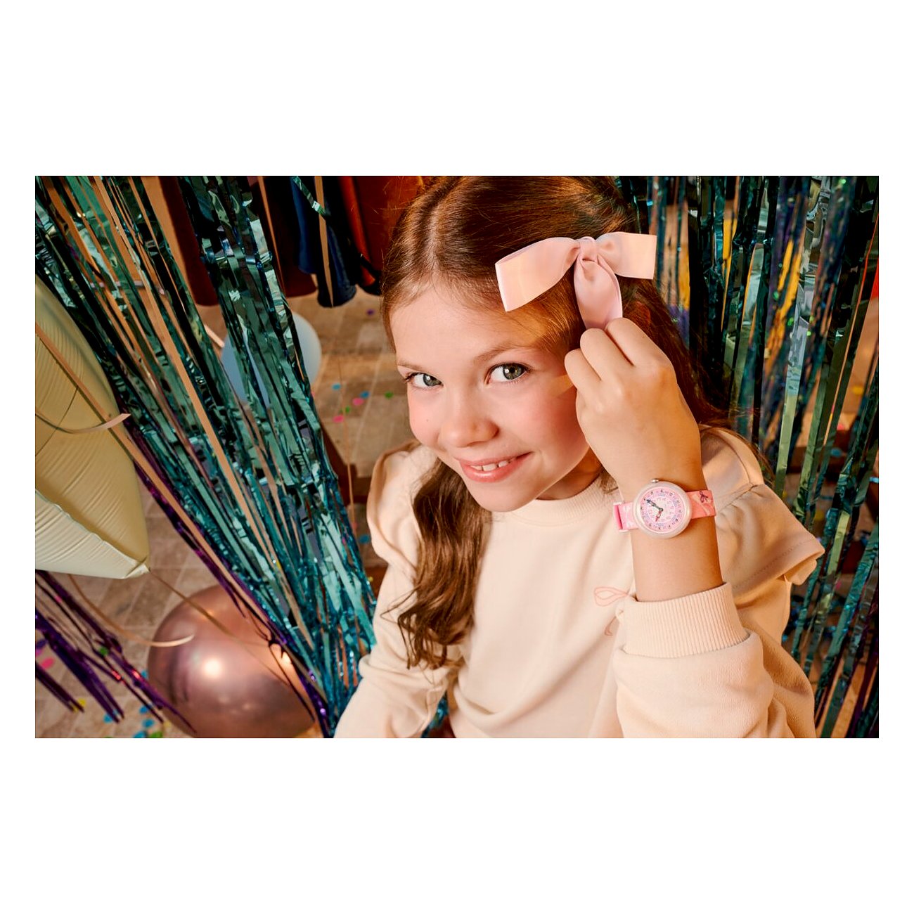 Ein glückliches Mädchen mit langen, welligen Haaren und einem rosa Flik Flak Kunststoff-Kinderuhr am Handgelenk.