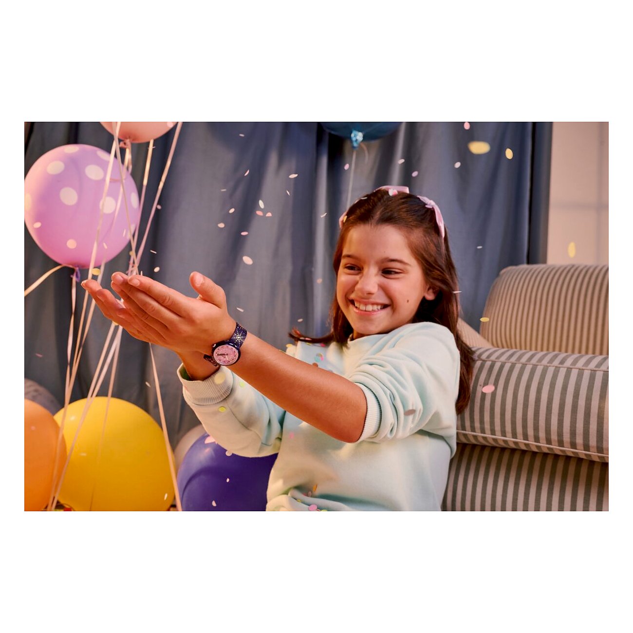 Ein lächelndes Mädchen fängt Konfetti mit ihren Händen. Sie trägt eine Flik Flak Kinder-/Jugenduhr.