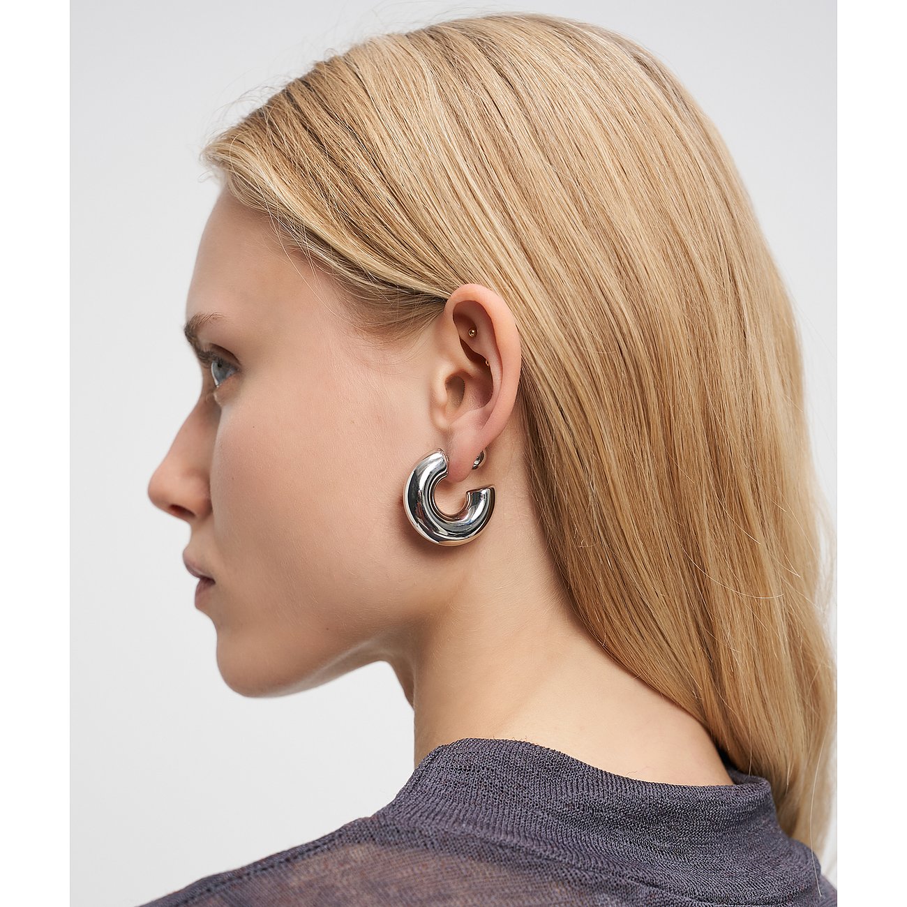 Nahaufnahme einer Frau mit glänzenden, silberfarbenen Liebeskind Edelstahl-Ohrringen in C-Form an ihrem rechten Ohr.