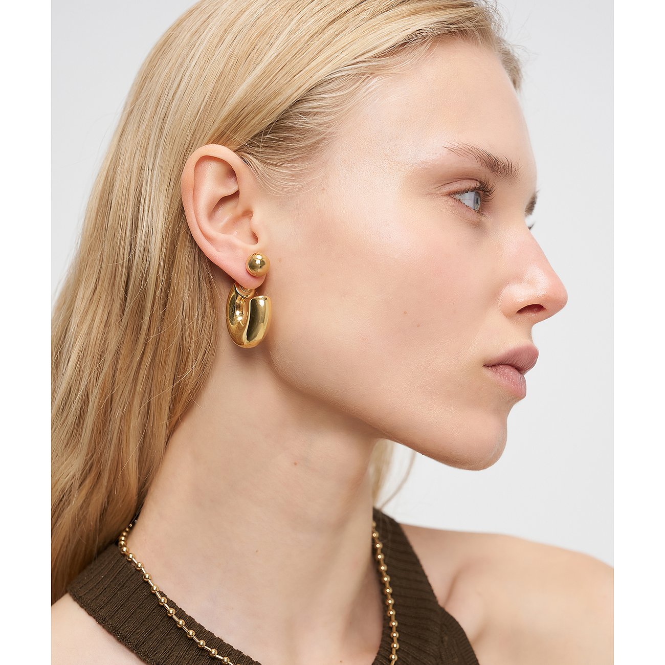 Close-up van de gouden Liebeskind oorbel van roestvrij staal, gedragen aan één oor.