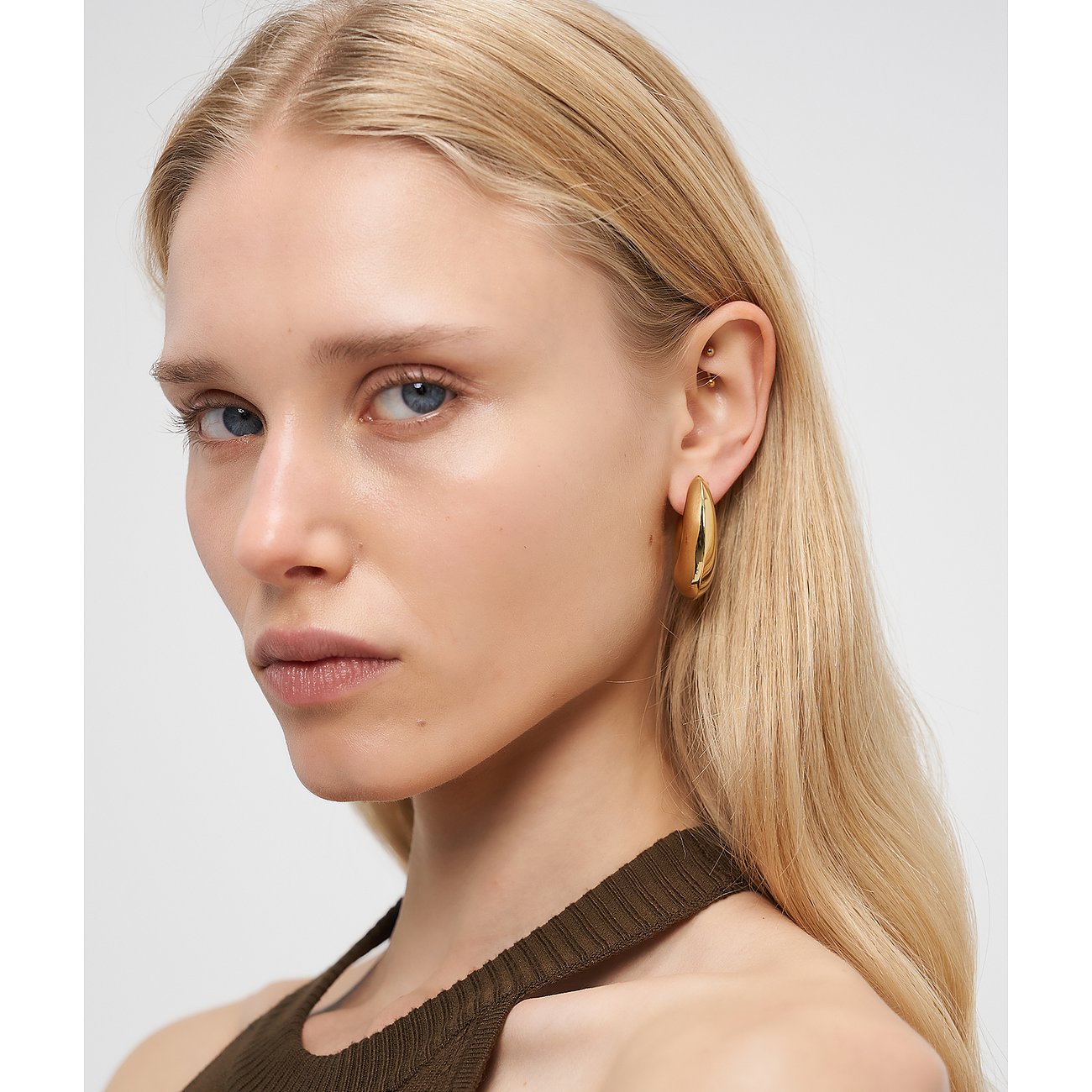 Nahaufnahme einer Frau, die einen einzelnen goldenen Liebeskind Edelstahl Ohrschmuck trägt.