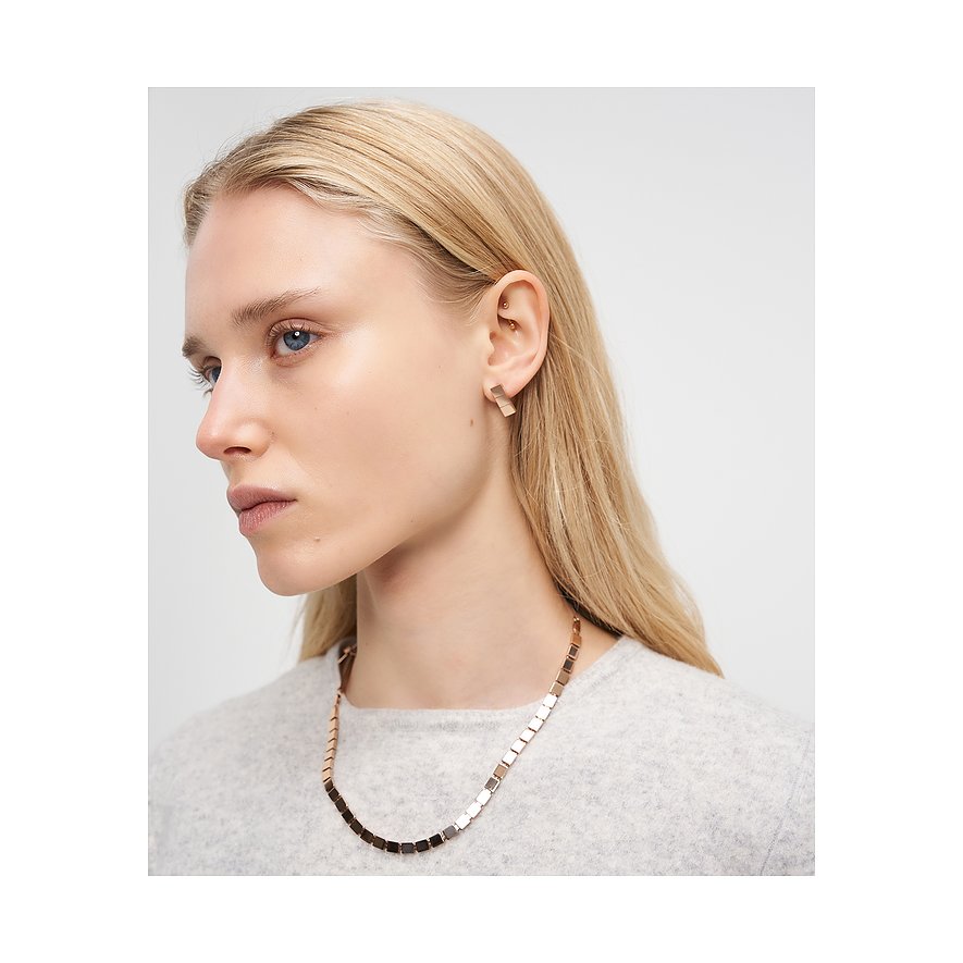 Blonde Frau, die das Liebeskind Halsschmuck aus Edelstahl mit quadratischen Gliedern und passende Ohrringe trägt.