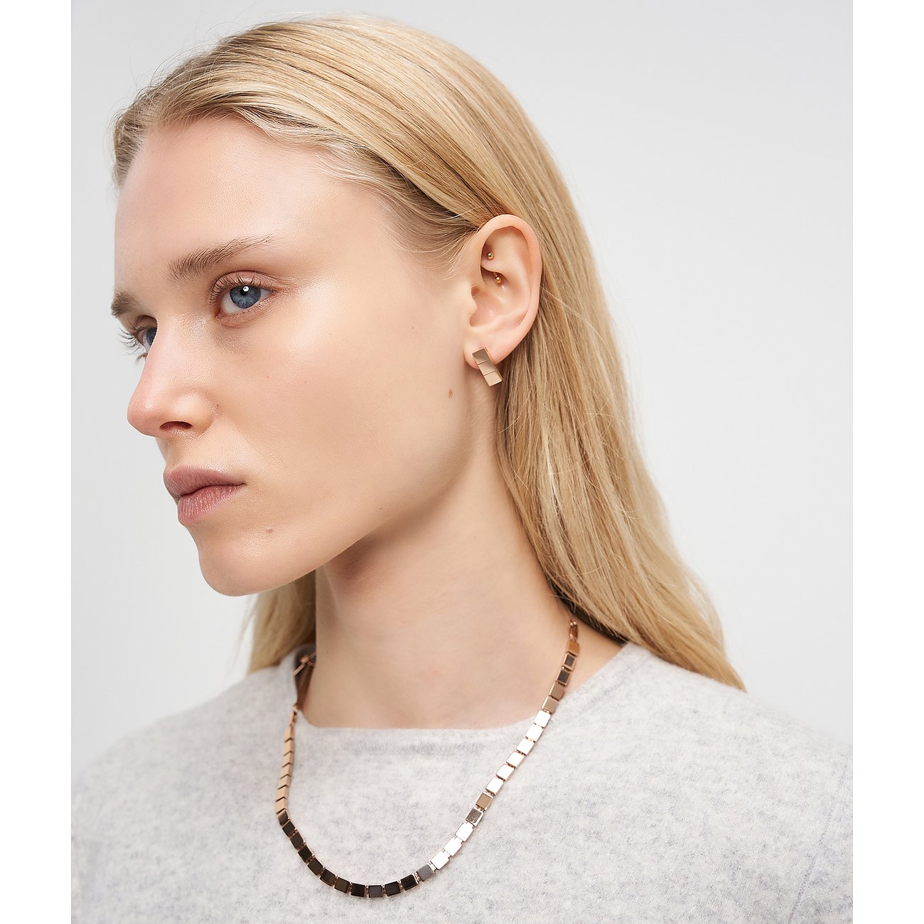 Blonde Frau, die das Liebeskind Halsschmuck aus Edelstahl mit quadratischen Gliedern und passende Ohrringe trägt.