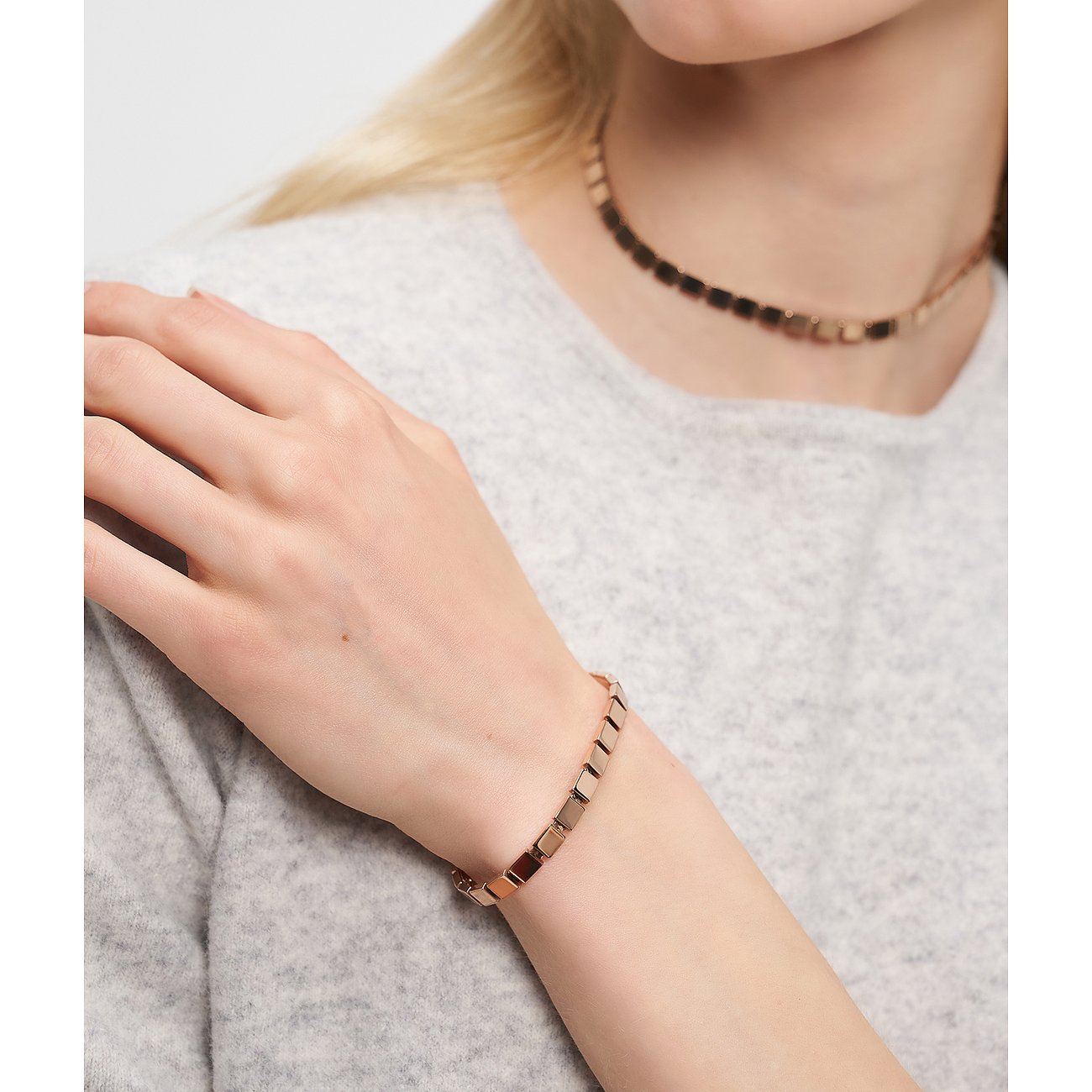 Roséguld Liebeskind-armband med kubformade länkar på kvinnas handled. Matchande halsband i bakgrunden.