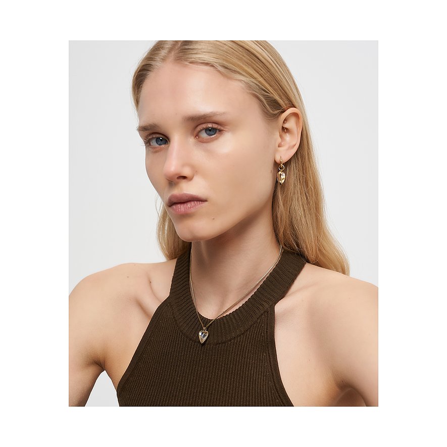 Närbild på en blond kvinna med ett Liebeskind-halsband och hjärtformade örhängen i guldfärgat rostfritt stål.