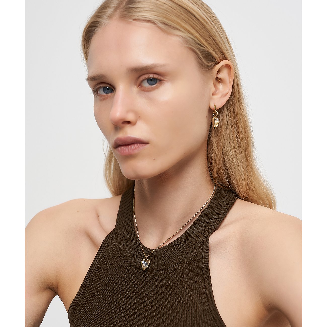 Närbild på en blond kvinna med ett Liebeskind-halsband och hjärtformade örhängen i guldfärgat rostfritt stål.