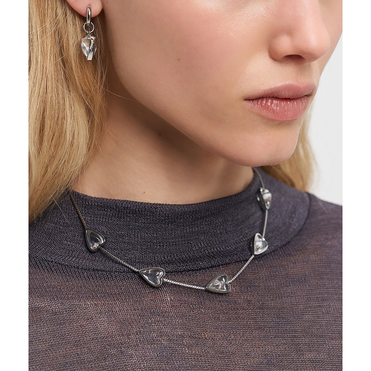 Primo piano di una donna con una collana Liebeskind in acciaio inossidabile e gemme chiare a forma di cuore.