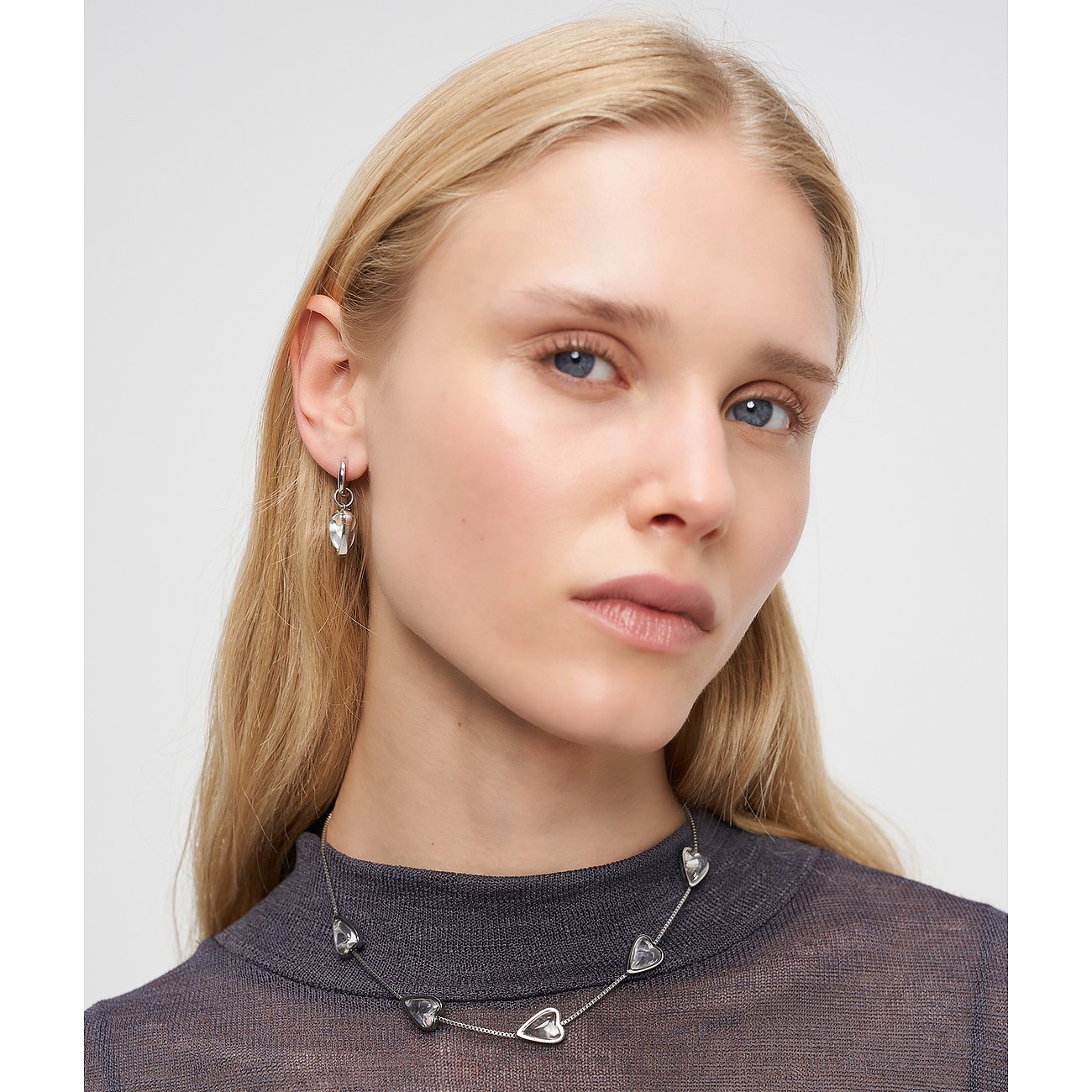 Primo piano di donna con collana Liebeskind in acciaio inox con ciondoli a cuore e orecchini abbinati.