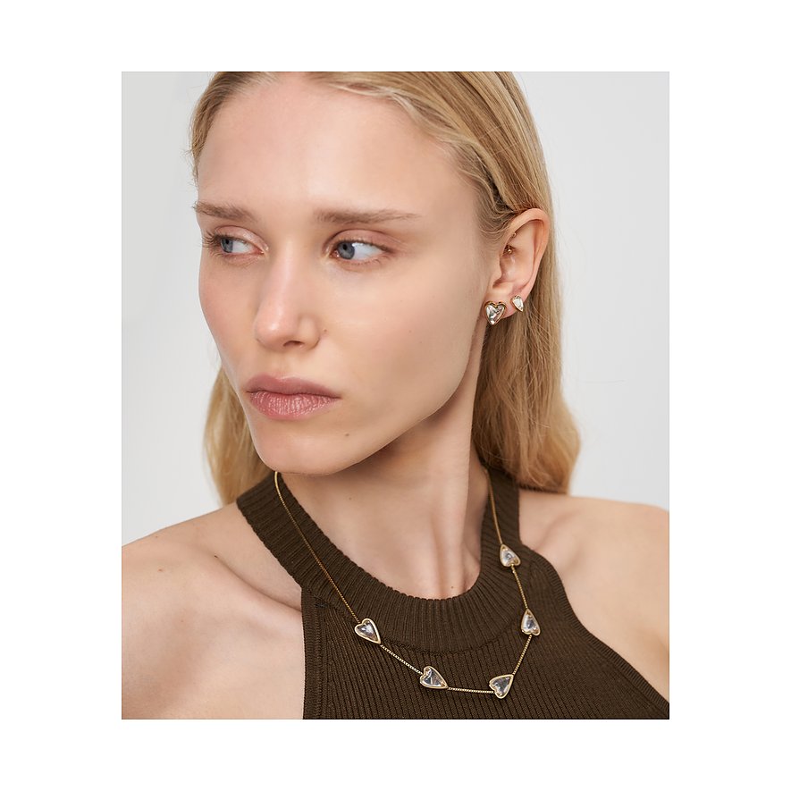 Nahaufnahme einer Frau mit goldenen Liebeskind Ohrsteckern und passender Halskette mit klaren herzförmigen Schmucksteinen.