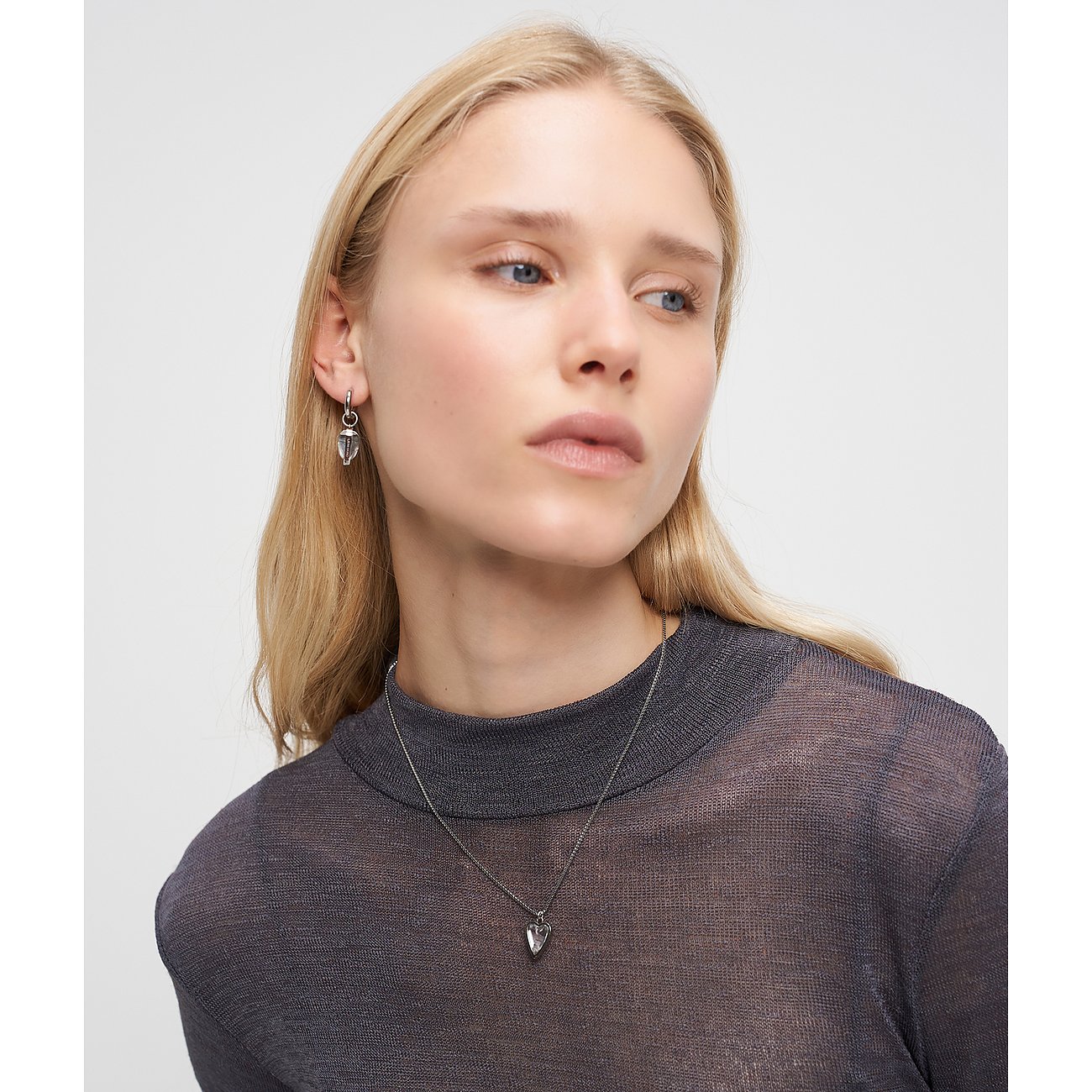 En model bærer Liebeskind øreringe og en matchende halskæde i rustfrit stål med en klar sten.