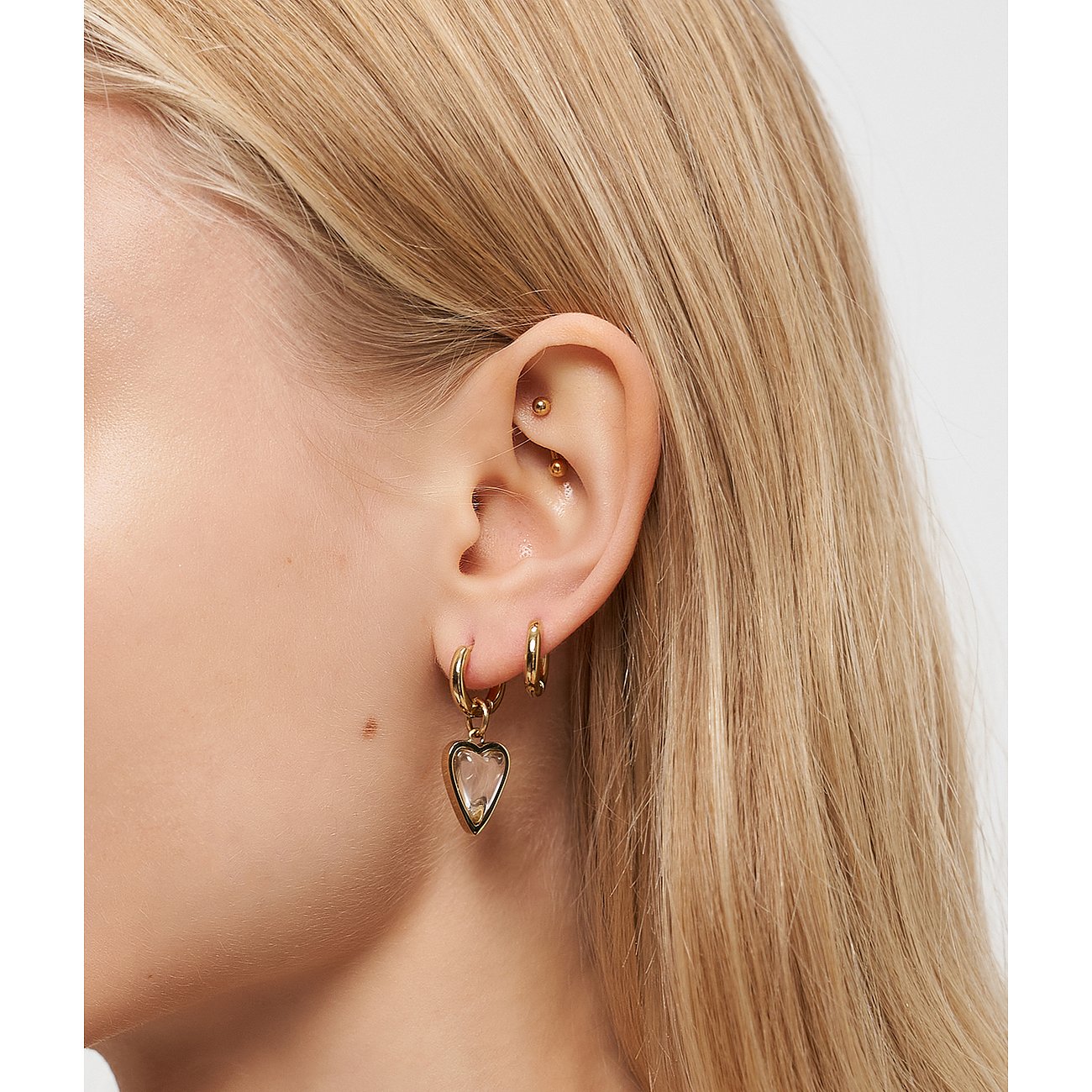 Ein blondes Ohr trägt einen Liebeskind Edelstahl Ohrring mit einem herzförmigen, klaren Steinanhänger