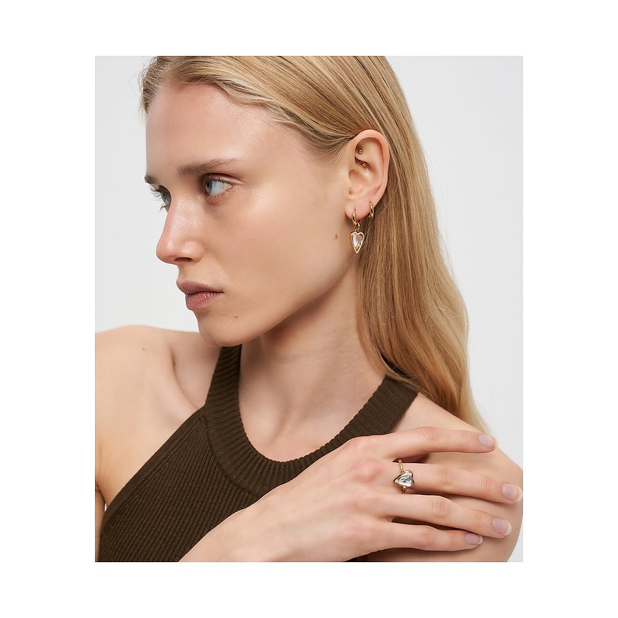 Nahaufnahme einer Frau, die goldfarbene Liebeskind Edelstahl-Ohrhaken mit herzförmigem Stein und einen passenden Ring trägt.