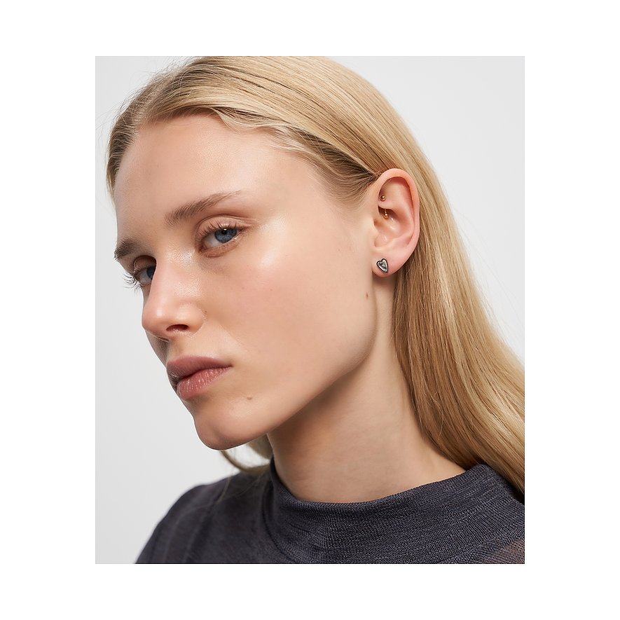 Modell bär Liebeskind öronsmycke i rostfritt stål i hjärtform på höger öra, med slätt blont hår.