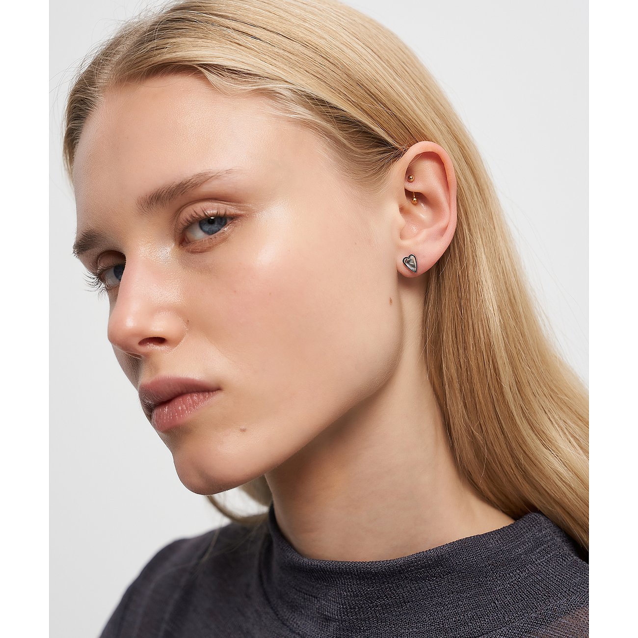 Modell bär Liebeskind öronsmycke i rostfritt stål i hjärtform på höger öra, med slätt blont hår.