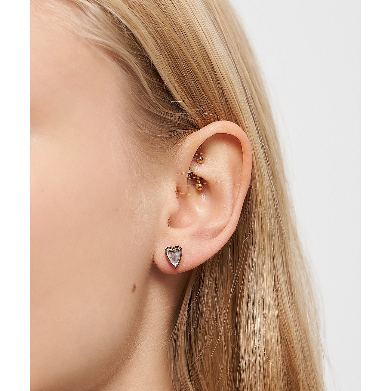 Nahaufnahme eines Ohres mit Liebeskind Edelstahlohrschmuck in Herzform. Der Ohrring ist hell schimmernd.