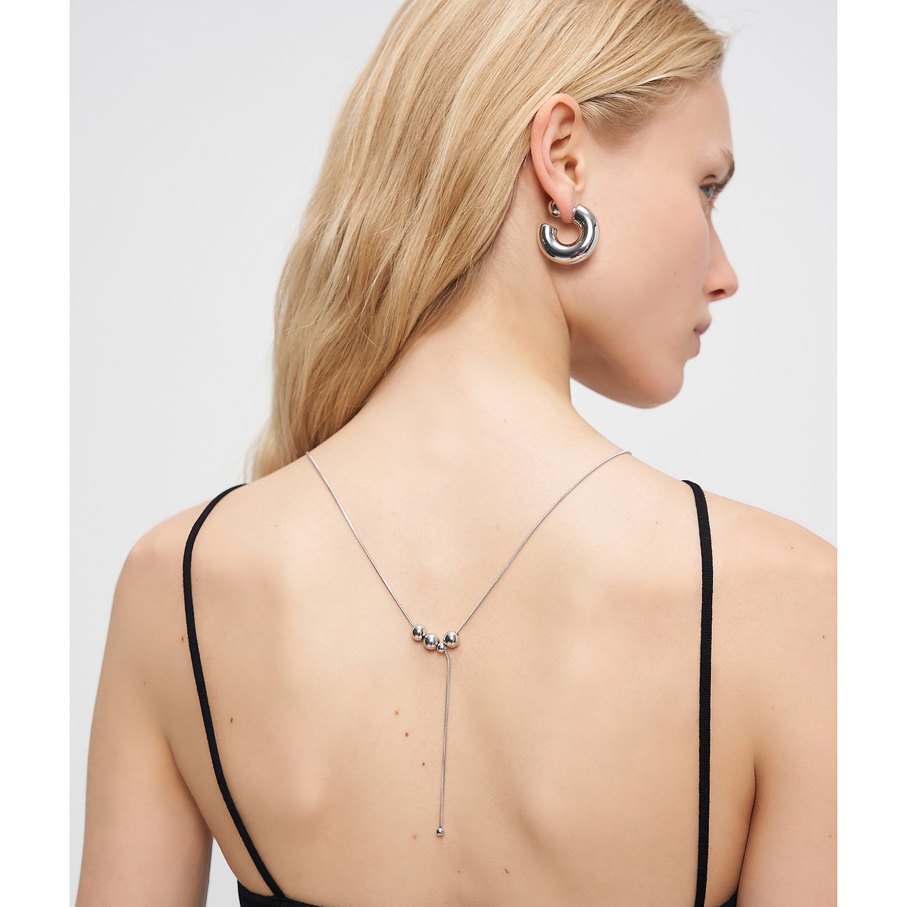 Vue arrière d'une femme aux longs cheveux blonds, portant un collier Liebeskind ouvert en acier avec trois perles.