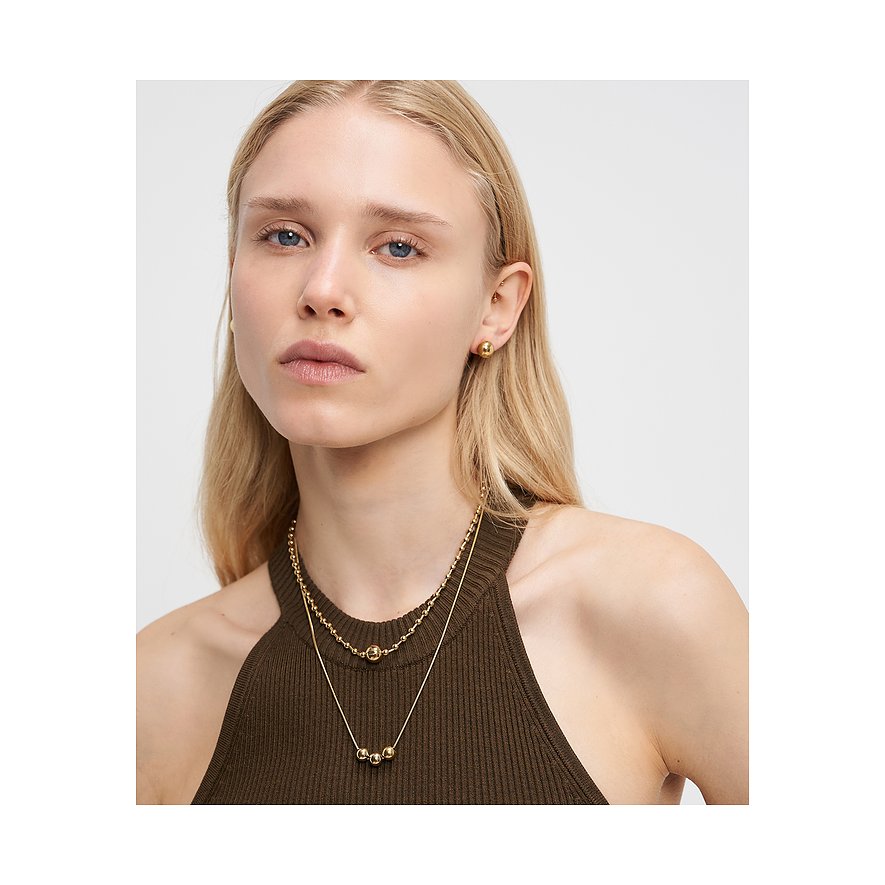 Le mannequin porte deux colliers Liebeskind en acier inoxydable doré et des boucles d'oreilles assorties.