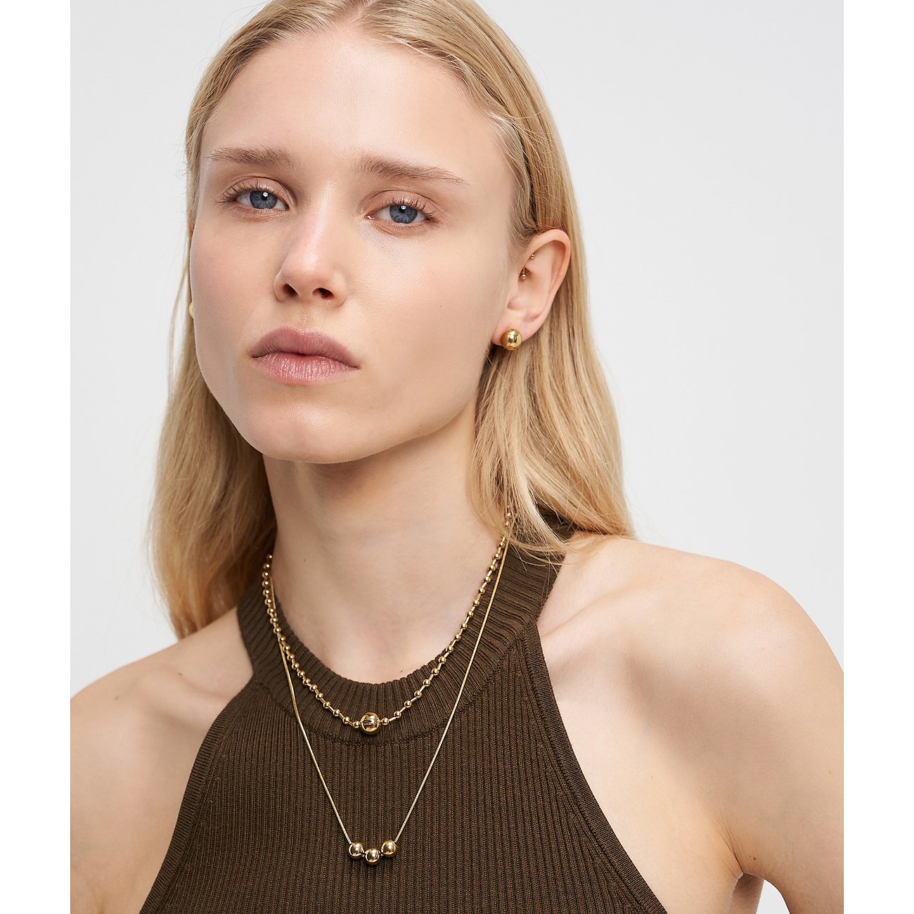 Le mannequin porte deux colliers Liebeskind en acier inoxydable doré et des boucles d'oreilles assorties.