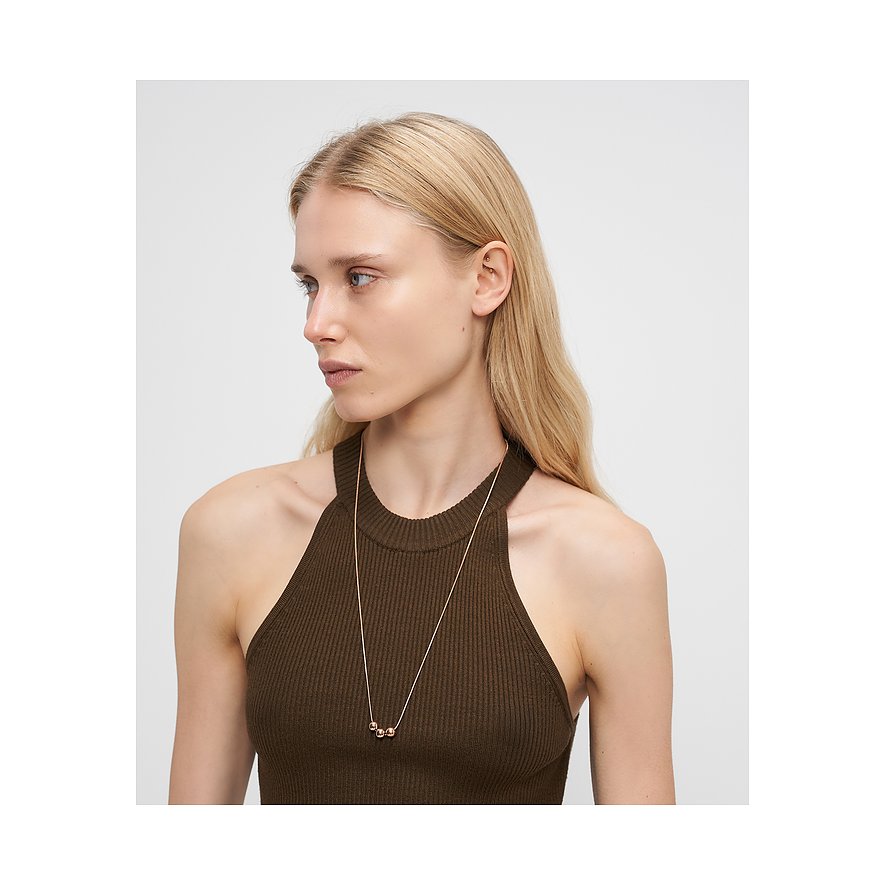 Nahaufnahme einer Frau, die eine Liebeskind Halskette aus roségoldfarbenem Edelstahl mit drei Kugeln trägt.