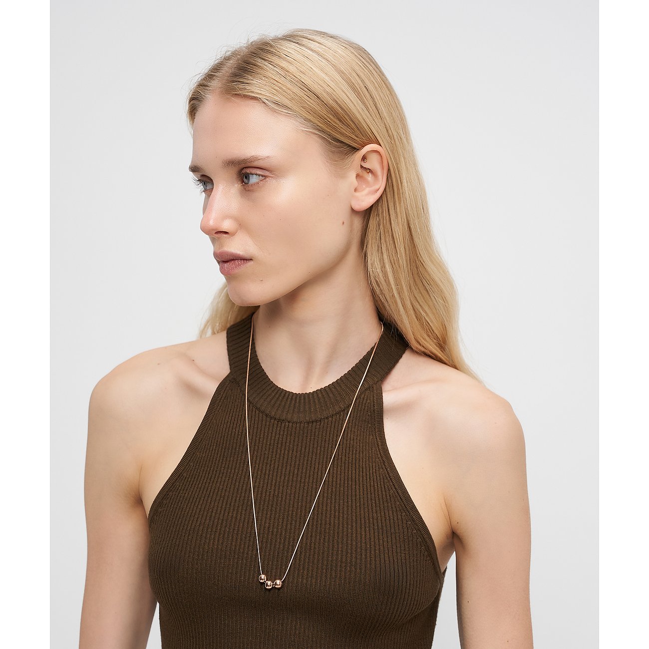 Nahaufnahme einer Frau, die eine Liebeskind Halskette aus roségoldfarbenem Edelstahl mit drei Kugeln trägt.