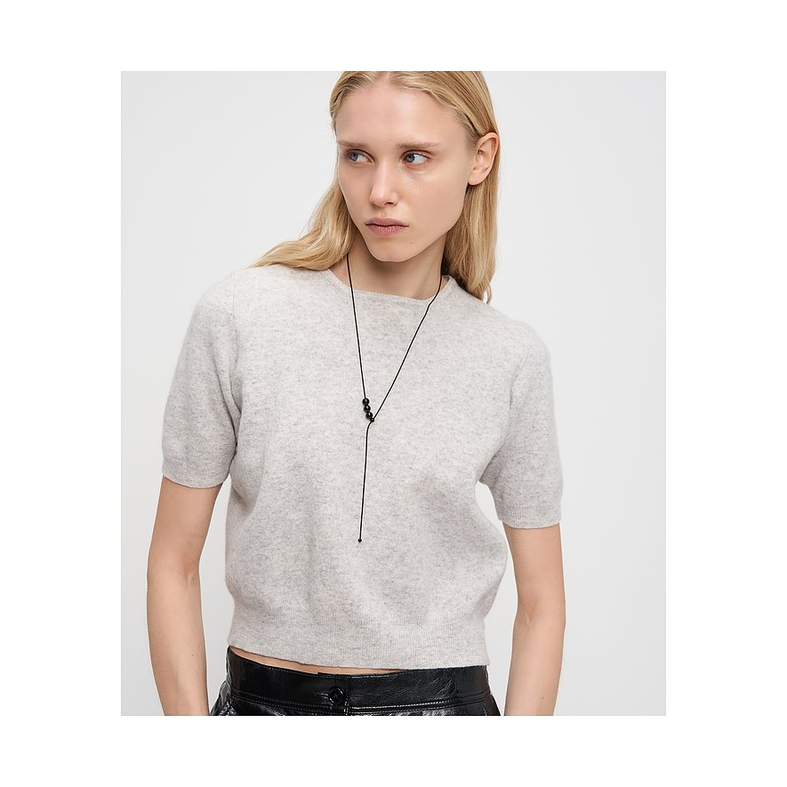 En blond modell bär ett långt, svart Liebeskind-halsband i rostfritt stål med tre svarta pärlor framtill.