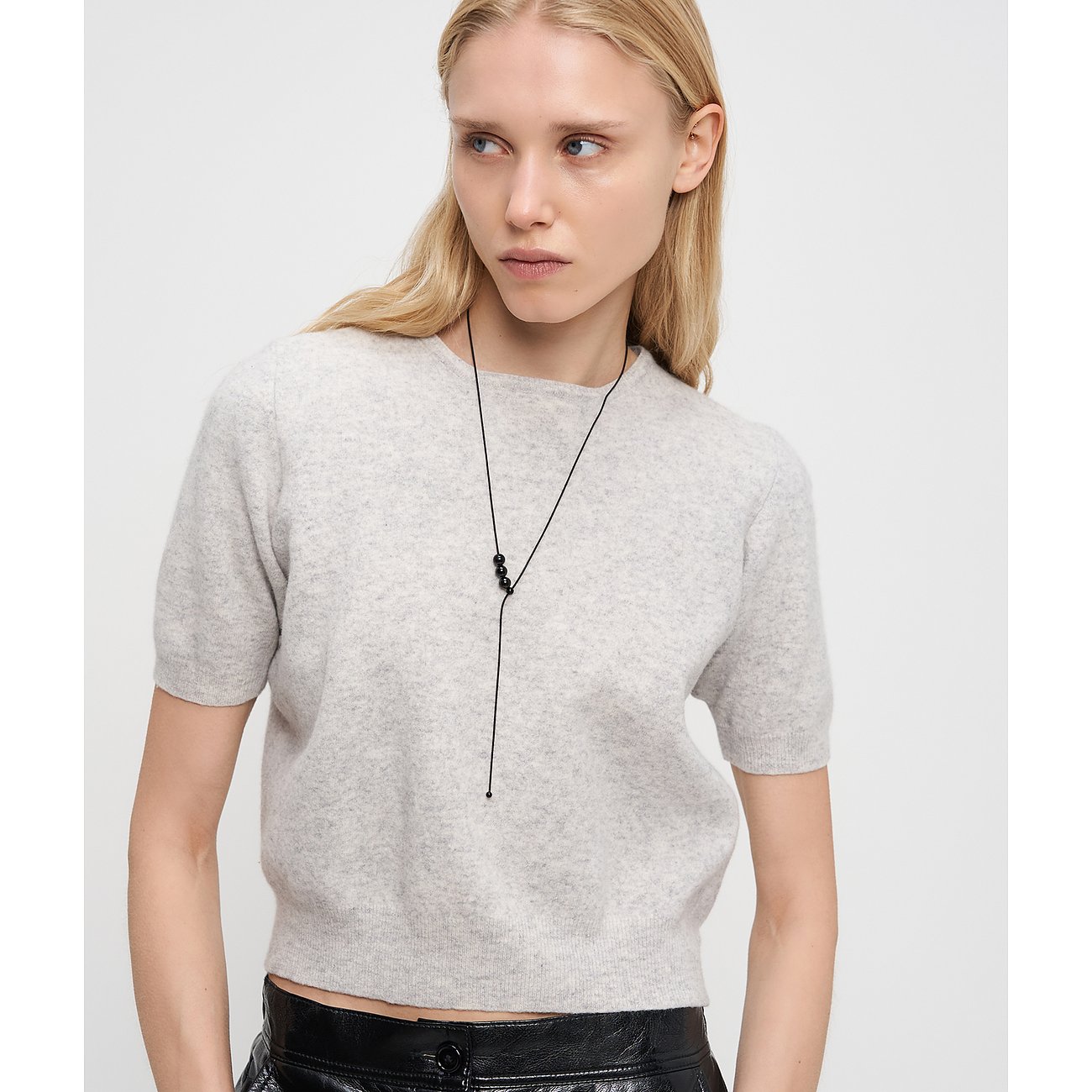 En blond modell bär ett långt, svart Liebeskind-halsband i rostfritt stål med tre svarta pärlor framtill.