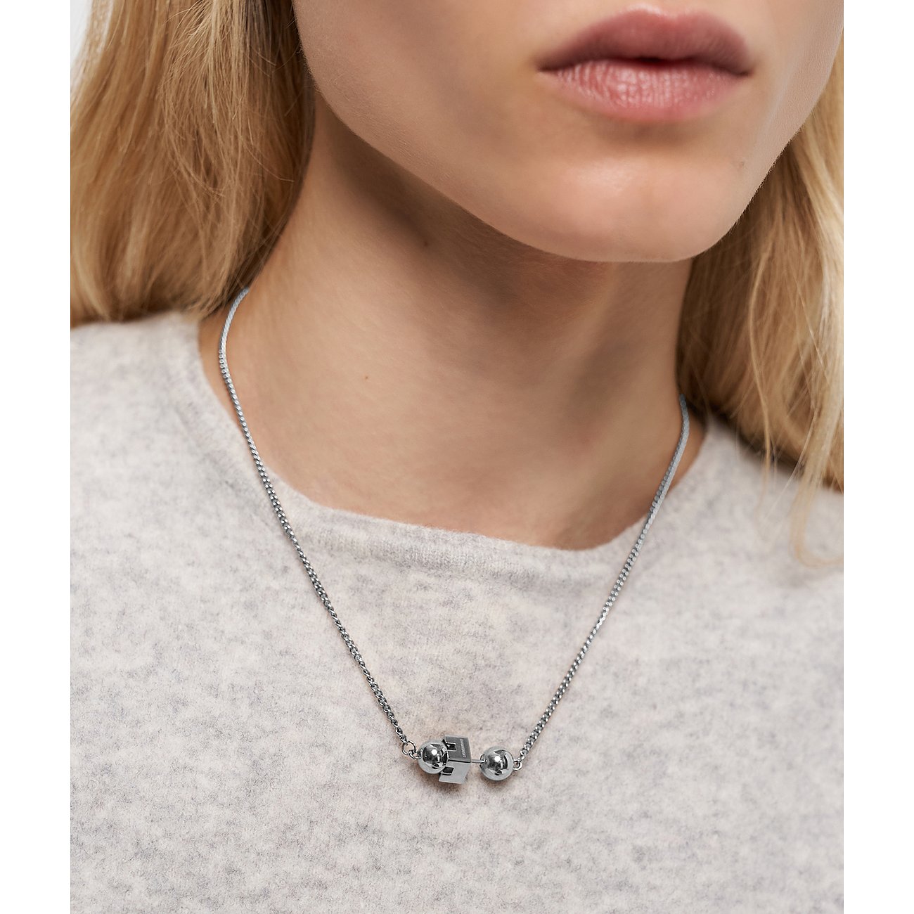 Närbild av en kvinna som bär ett Liebeskind halsband i rostfritt stål med tre kulor runt halsen.